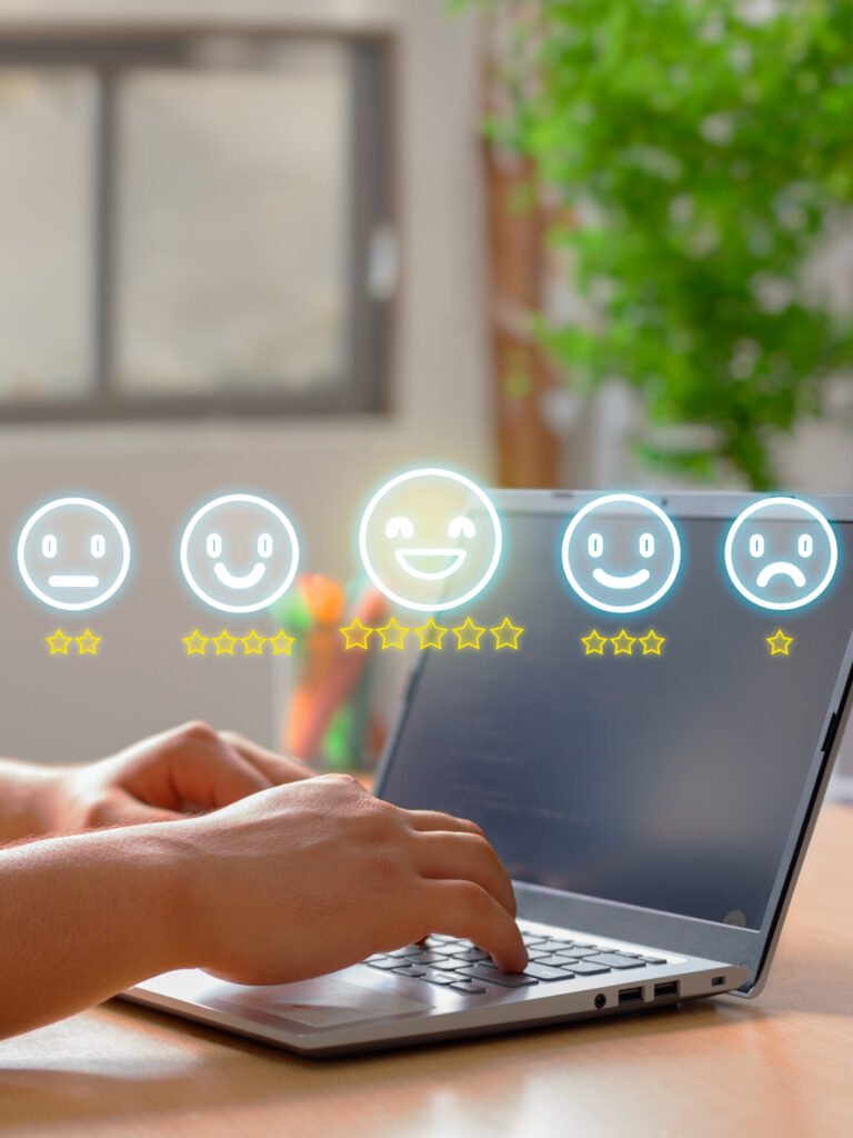 Hands typing on a laptop with five rating smiley faces, ranging from sad to happy, and highlighted stars above the keyboard, representing an online feedback or review system that showcases important website trust signals for any small business.
